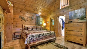 A cozy log cabin bedroom with a bed, dresser, and a small table.