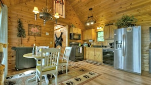 A cozy cabin-style kitchen with wooden walls, a dining table with chairs, a refrigerator, and a microwave.