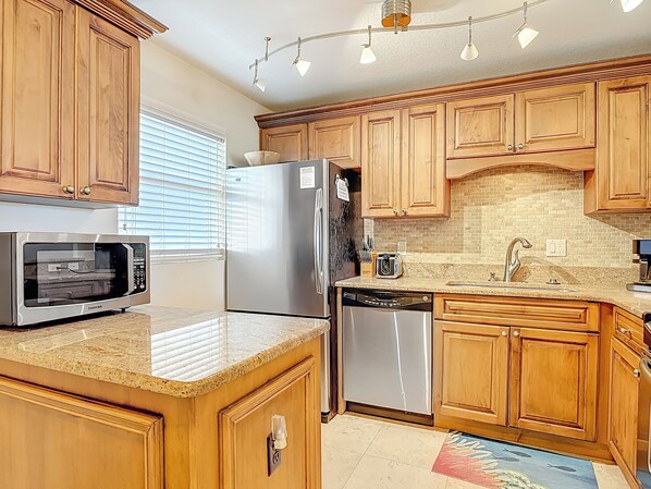 A kitchen with wooden cabinets, a stainless steel refrigerator, a microwave, a dishwasher, and a tiled backsplash.
