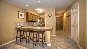 A kitchen with a central island, bar stools, wooden cabinets, a clock, and a door.