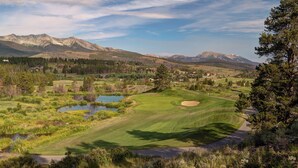A golf course with a pond, surrounded by mountains and trees.