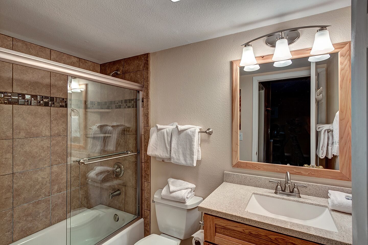 A modern bathroom with a glass-enclosed shower, a vanity with a sink, and a mirror with three lights.