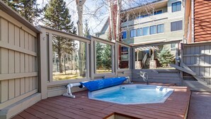 A hot tub area with a wooden deck, a covered seating area, and a view of a residential building in the background.