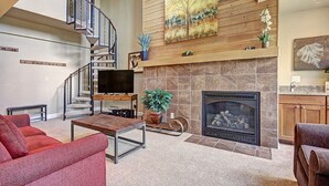 A spacious living room with a fireplace, a television, and a staircase leading to an upper level.