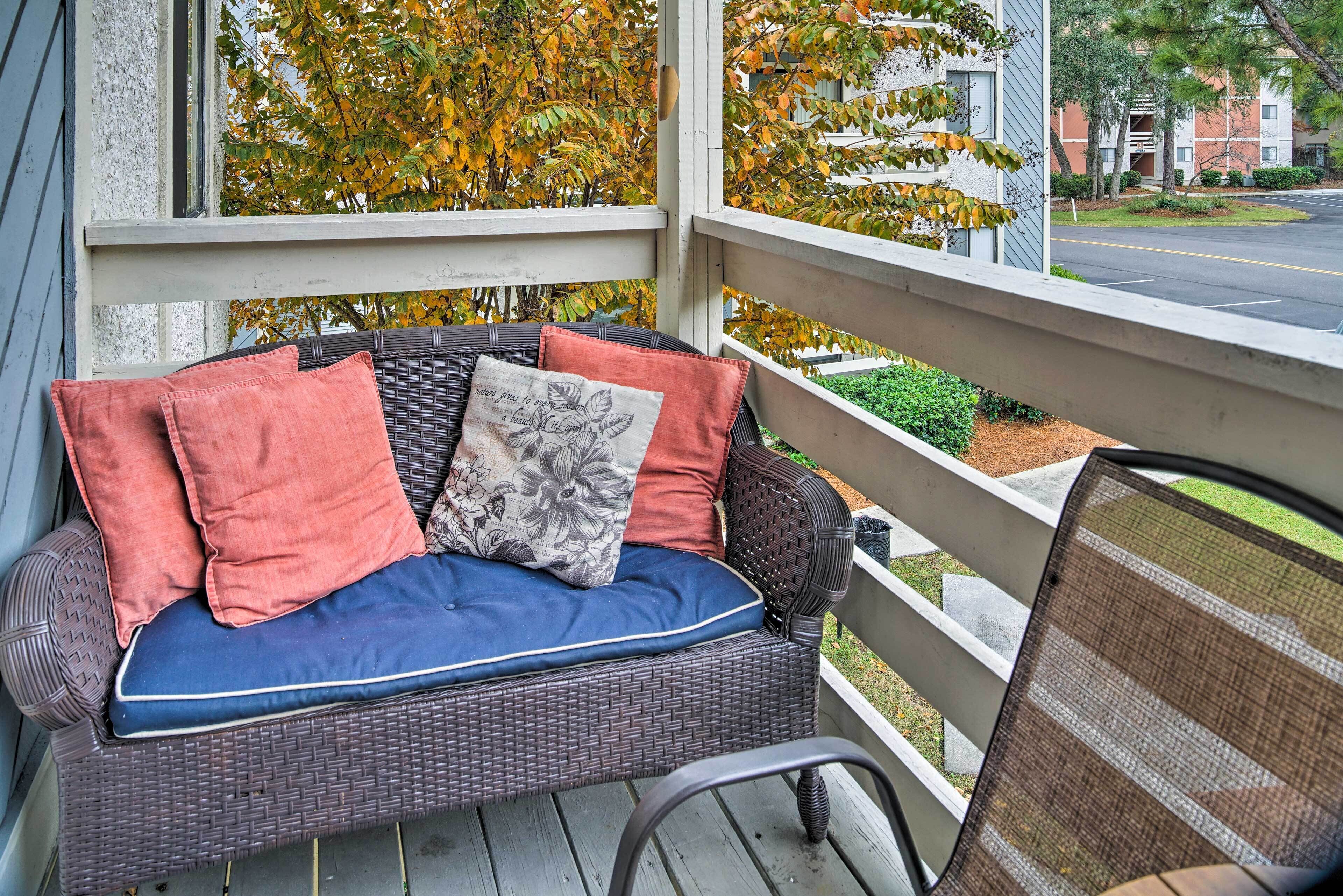Ein Korbsessel mit Kissen auf einer Veranda mit Blick auf eine Straße, gesäumt von Herbstlaub.