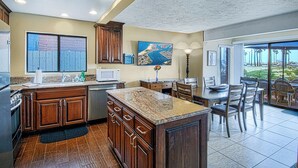 A kitchen with wooden cabinets, a granite countertop, and a dining area with chairs and a table. - Spacious lower oceanfront located within walking distance of the Balboa Pier fun (Newport Beach)
