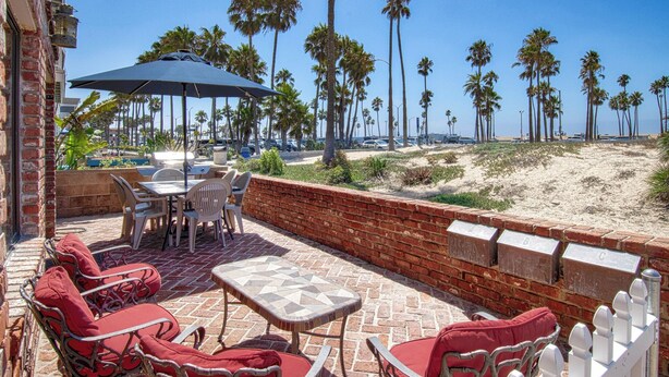 An outdoor patio with a brick wall, a table, chairs, and a large umbrella. - Spacious lower oceanfront located within walking distance of the Balboa Pier fun (Newport Beach)