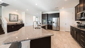 A modern kitchen with granite countertops, stainless steel appliances, and dark cabinetry. - Luxurious Villa with Tiki Themed Game Room at Encore (Kissimmee)