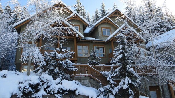 A large, multi-story wooden house with a stone foundation, surrounded by snow-covered trees. - Ski-In/Ski-Out | Mountain Views | Private Hot Tub | Modern 3BR | Managed by Aloha Whistler (Whistler)