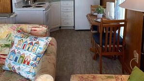 Une cuisine compacte équipée d’une cuisinière, d’un four à micro-ondes et d’un réfrigérateur. On y trouve une table à manger avec des chaises, et un ventilateur de plafond au-dessus.