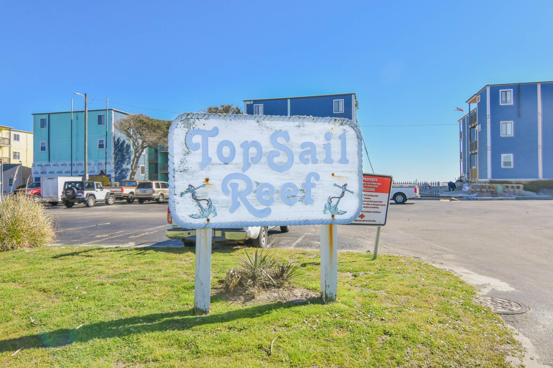 A sign for Topsail Reef with a parking area and buildings in the background.