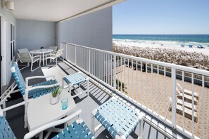 Un balcon agrémenté de meubles blancs et bleus, une petite table avec une plante, et une vue sur la plage et l’océan.