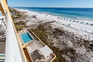 A hotel with a pool, beach view, and beach umbrellas.