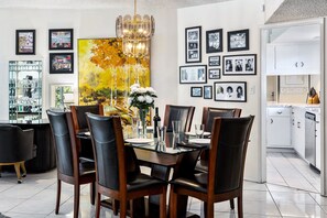 Uma área de refeições com mesa de vidro, cadeiras de couro preto e uma pintura grande na parede.
