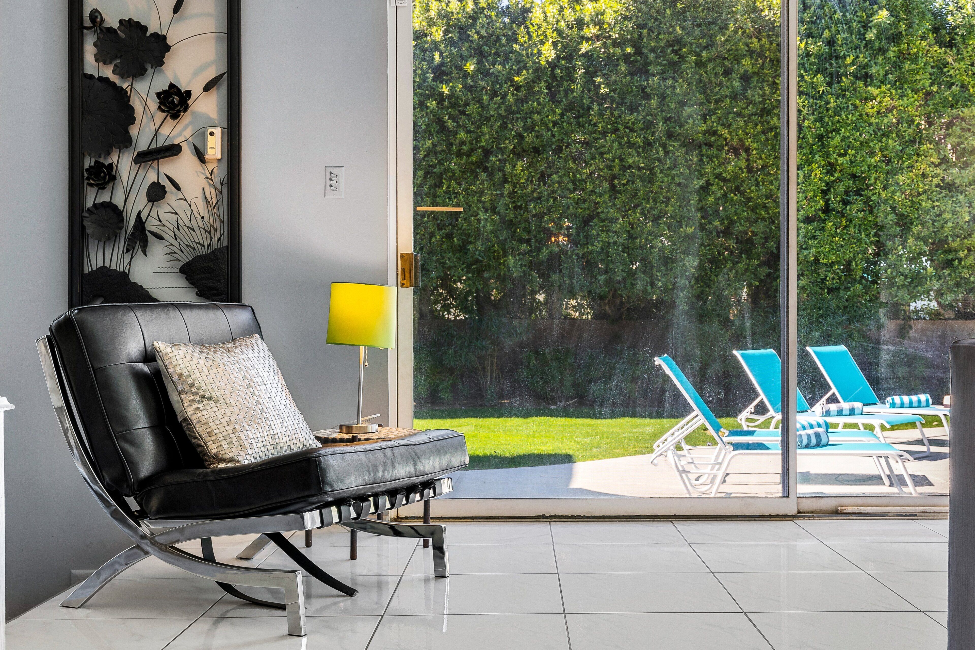 A modern living room with a black leather sofa, a lamp, and a view of a pool and garden through large glass doors.