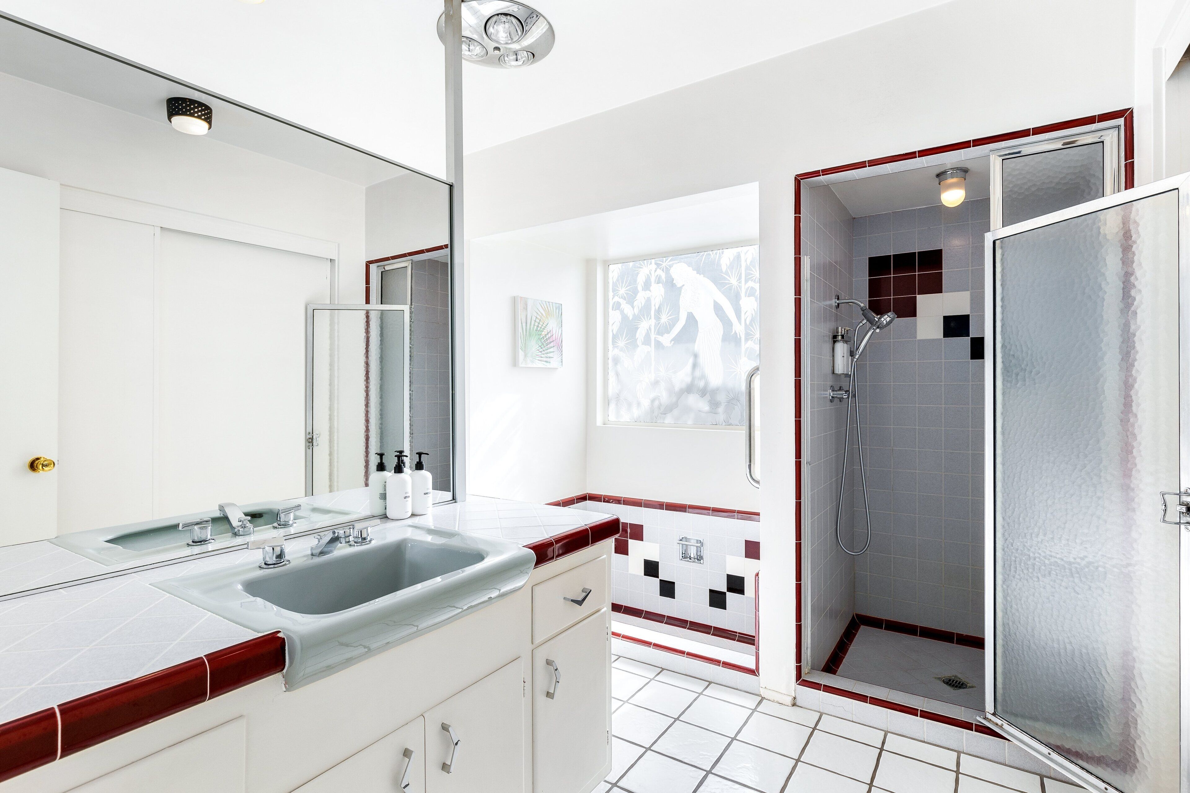Une salle de bain avec un grand miroir, deux lavabos, une douche et une fenêtre.