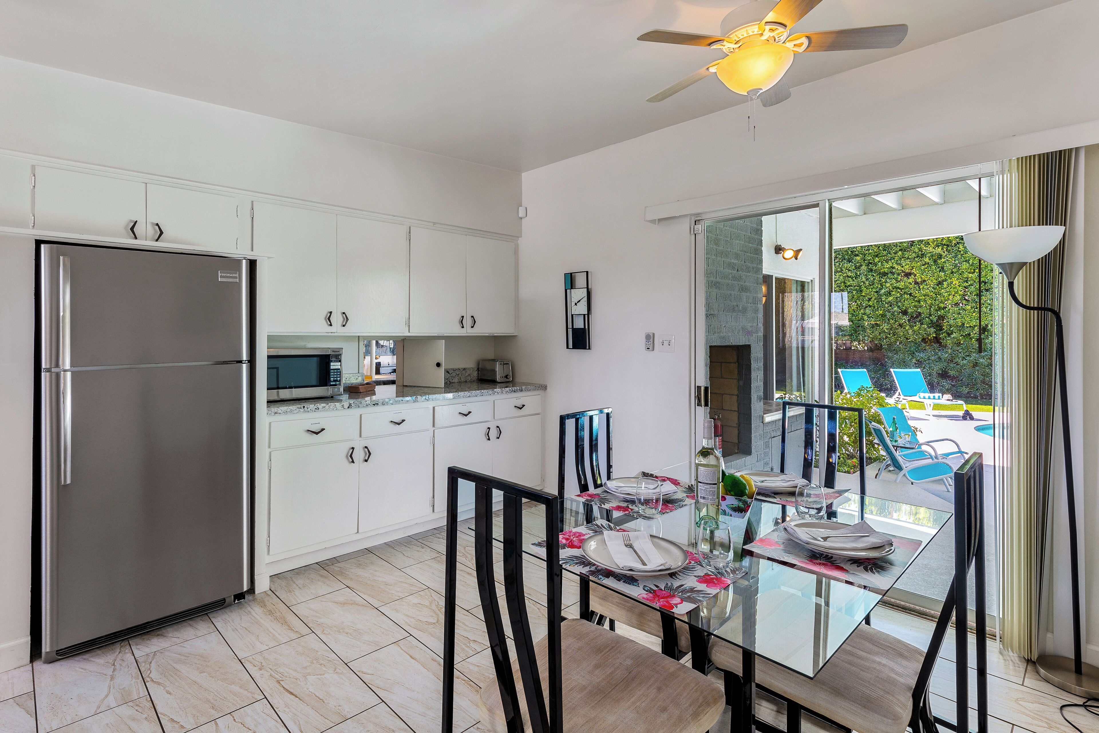 A modern kitchen with white cabinets, a stainless steel refrigerator, and a dining area with a glass table and chairs.