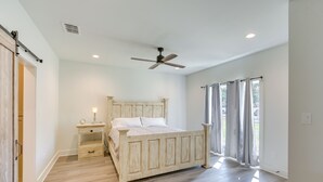 Un dormitorio con cama, mesita de noche, ventilador de techo y ventana con cortinas.