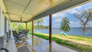 Un espacio al aire libre cubierto con un banco, sillas y vistas a un lago y árboles.