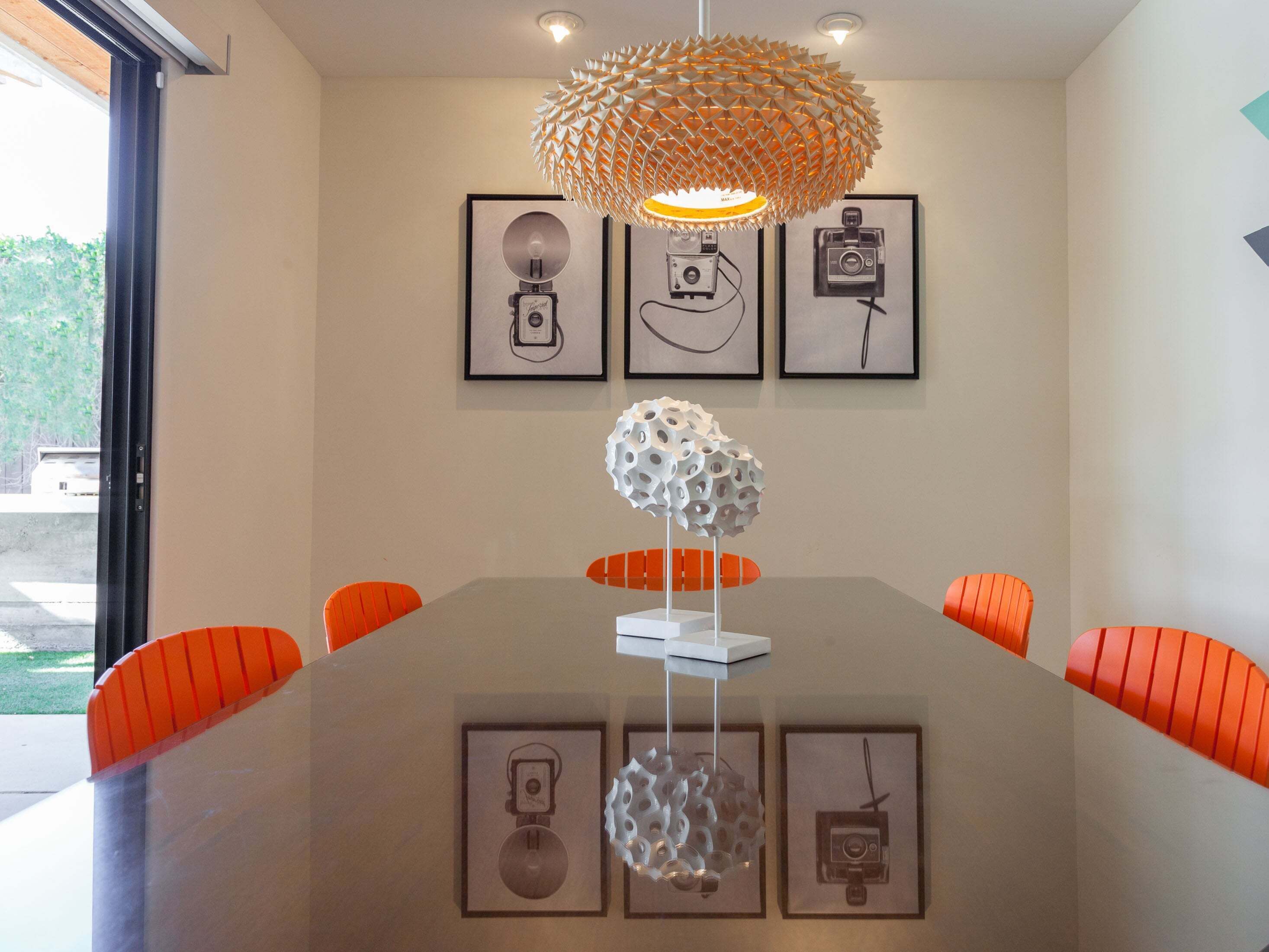 A conference room with a glass table, orange chairs, a unique spherical light fixture, and framed pictures on the wall.