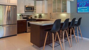 A modern kitchen with stainless steel appliances, a central island with bar stools, and a decorative wall piece. - Atomic Ranch Heaven - Pool, Spa & Mountain Views (Palm Springs)