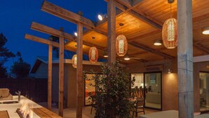 An outdoor patio with a fire feature, wooden benches, and hanging pendant lights. - Atomic Ranch Heaven - Pool, Spa & Mountain Views (Palm Springs)