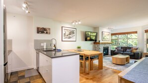 Een moderne keuken met een geïntegreerd eiland, een eethoek met een houten tafel, een open haard en een gezellige zithoek met een bank en een salontafel.