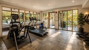 Een fitnessruimte met cardioapparatuur, een loopband en een hometrainer.