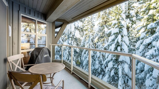 Een balkon met uitzicht op besneeuwde bomen, een houten tafel en een barbecue.