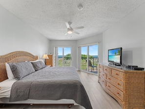 A bedroom with a bed, a television, a ceiling fan, and a balcony with a view.