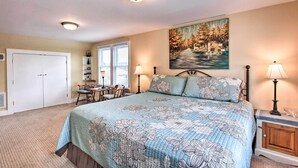 A bedroom with a large bed, two bedside lamps, a painting on the wall, a desk with a chair, and a closet.