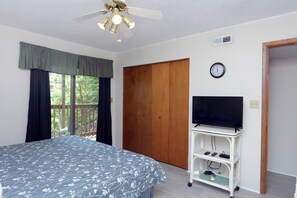 Un dormitorio con cama, televisor sobre un mueble, armario de madera y ventana con cortinas.