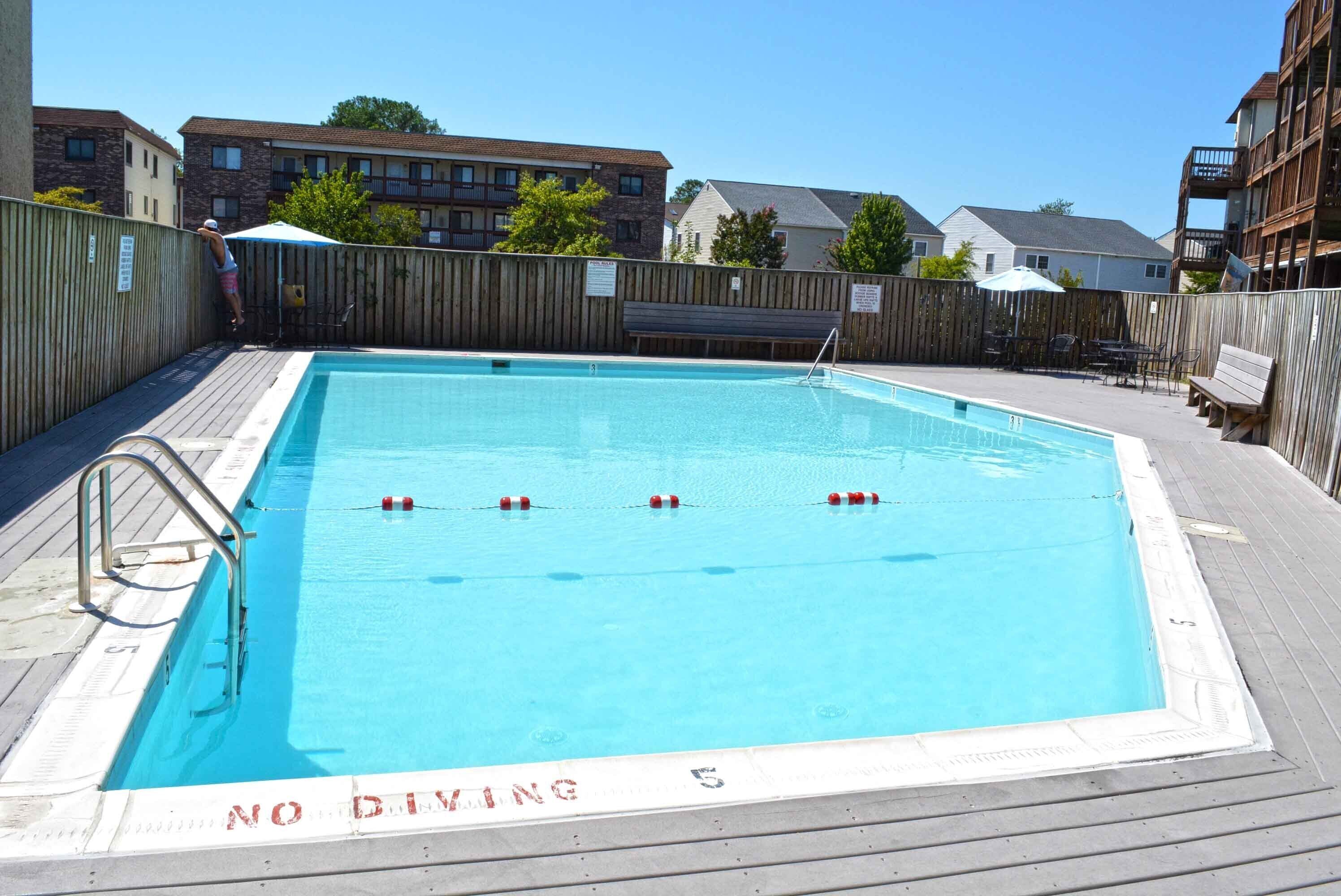 Une piscine rectangulaire entourée d’une terrasse en bois. On peut y voir trois bouées de sauvetage flottant à la surface de l’eau.