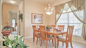 A dining room with a wooden table set for six, surrounded by six chairs. There is a chandelier hanging from the ceiling, and a framed picture on the wall. - 4 Mi to Disney: Kissimmee Group Getaway (Kissimmee)