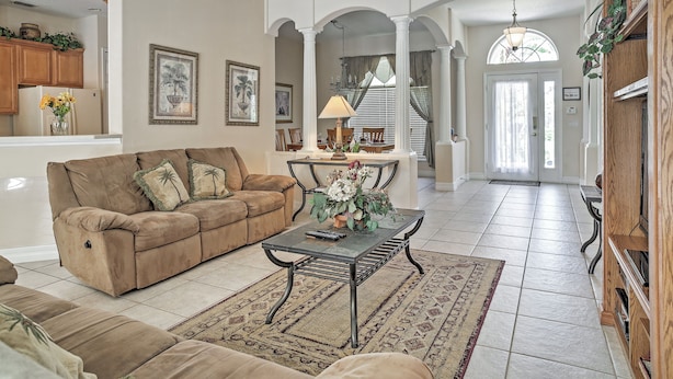 A spacious living room with a beige sofa, a coffee table, and a rug. There are framed pictures on the walls, a chandelier, and a wooden bookshelf. - 4 Mi to Disney: Kissimmee Group Getaway (Kissimmee)