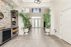 A hallway with a stone wall, a bookshelf, potted plants, and a modern kitchen area.