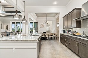 A modern kitchen with a large island, dark wooden cabinets, and a view to the outside.