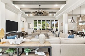 A spacious living room with a large sectional sofa, a flat-screen TV, and a dining area with a stone backsplash.