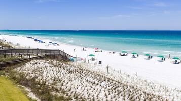 A beach with a wooden boardwalk, white sand, and clear blue water.
