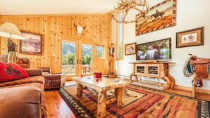 A rustic living room with wooden walls, a large wooden coffee table, leather sofas, and a mounted deer head.