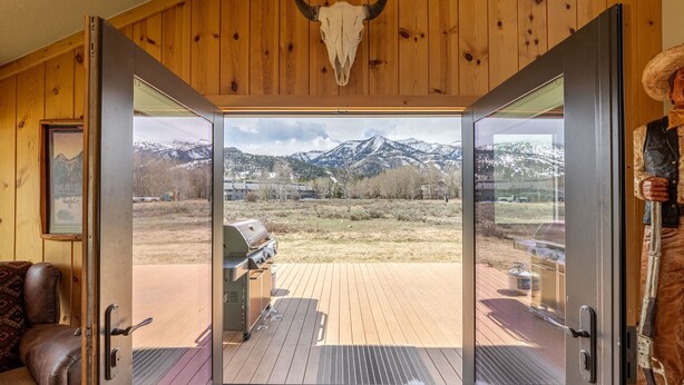 A room with wooden walls, a large glass door leading to an outdoor deck, a mounted bull skull, and a rustic decor including a cowboy hat.