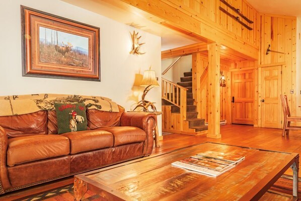 Un interior de madera con un sofá de cuero, un cuadro enmarcado, una lámpara y una escalera.