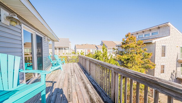 Een houten terras met turquoise Adirondack-stoelen, een leuning en uitzicht op naburige gebouwen.