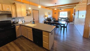 A modern kitchen with a central island, wooden cabinets, and a dishwasher. There is a dining area with a table and chairs, and a living room with a sofa and a fireplace. - Two Bedroom Condo @ Spring Brook Resort (Wisconsin Dells)