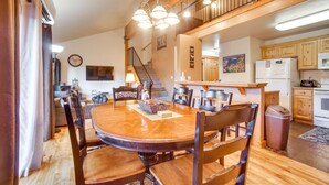 A spacious dining area with a wooden table and chairs, a chandelier, and a kitchen in the background.