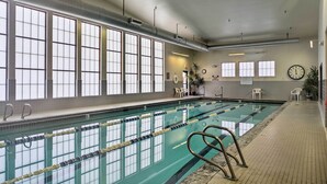 An indoor swimming pool with clear lanes, a clock on the wall, and large windows.