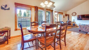 A dining area with a wooden table and chairs, a chandelier, and large windows with curtains.