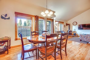 A dining area with a wooden table and chairs, a chandelier, and large windows with curtains. - McCall Vacation Rental ~ 1/2 Mi to Payette Lake! (McCall)