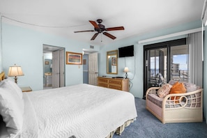 A hotel room with a bed, a dresser, a television, and a balcony with a view.