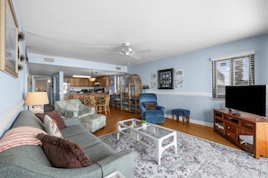 A living room with a sofa, a coffee table, a TV, and a dining area with chairs and a table.